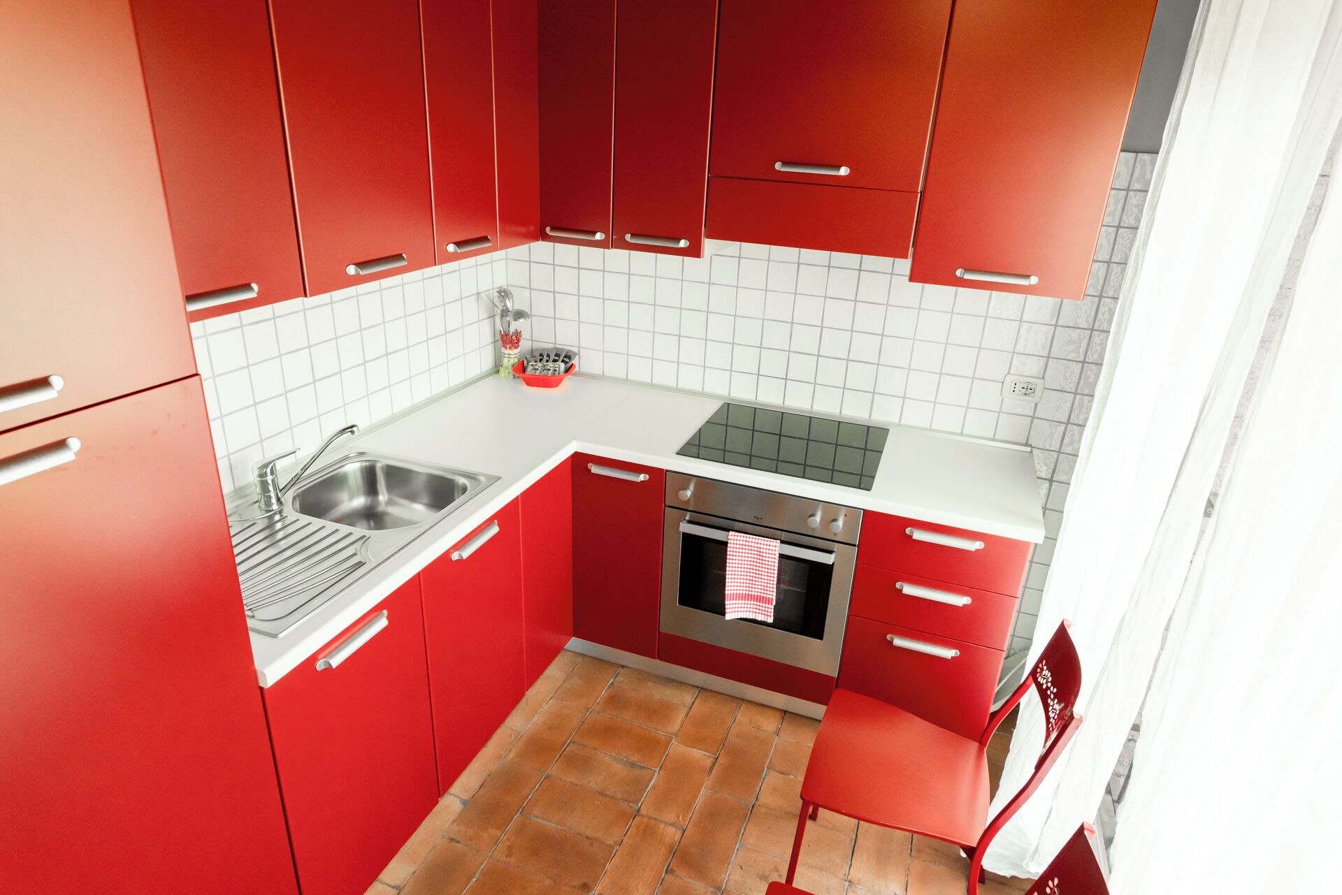Une cuisine de taille réduite avec des meubles rouges, un évier en acier inoxydable et un four encastré.
