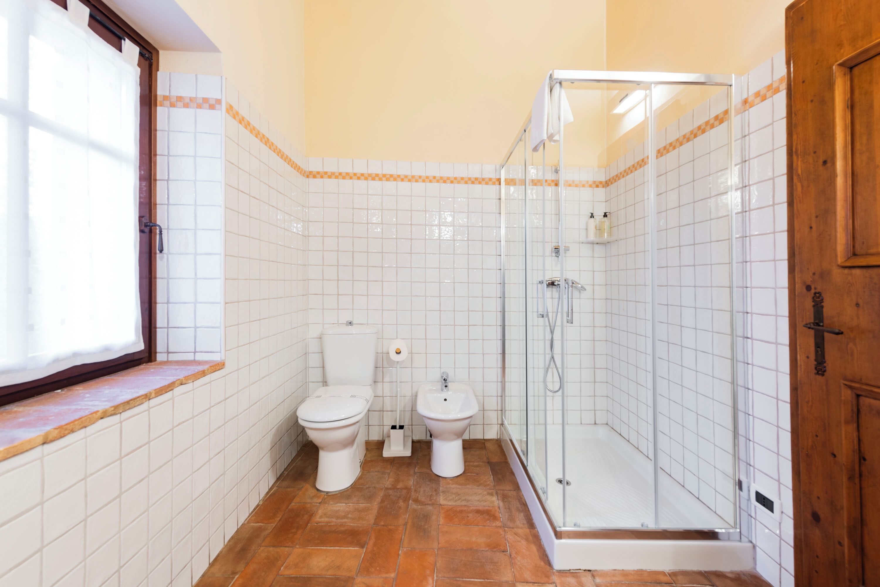 Un baño con dos inodoros, un bidé y una ducha con mampara de vidrio.
