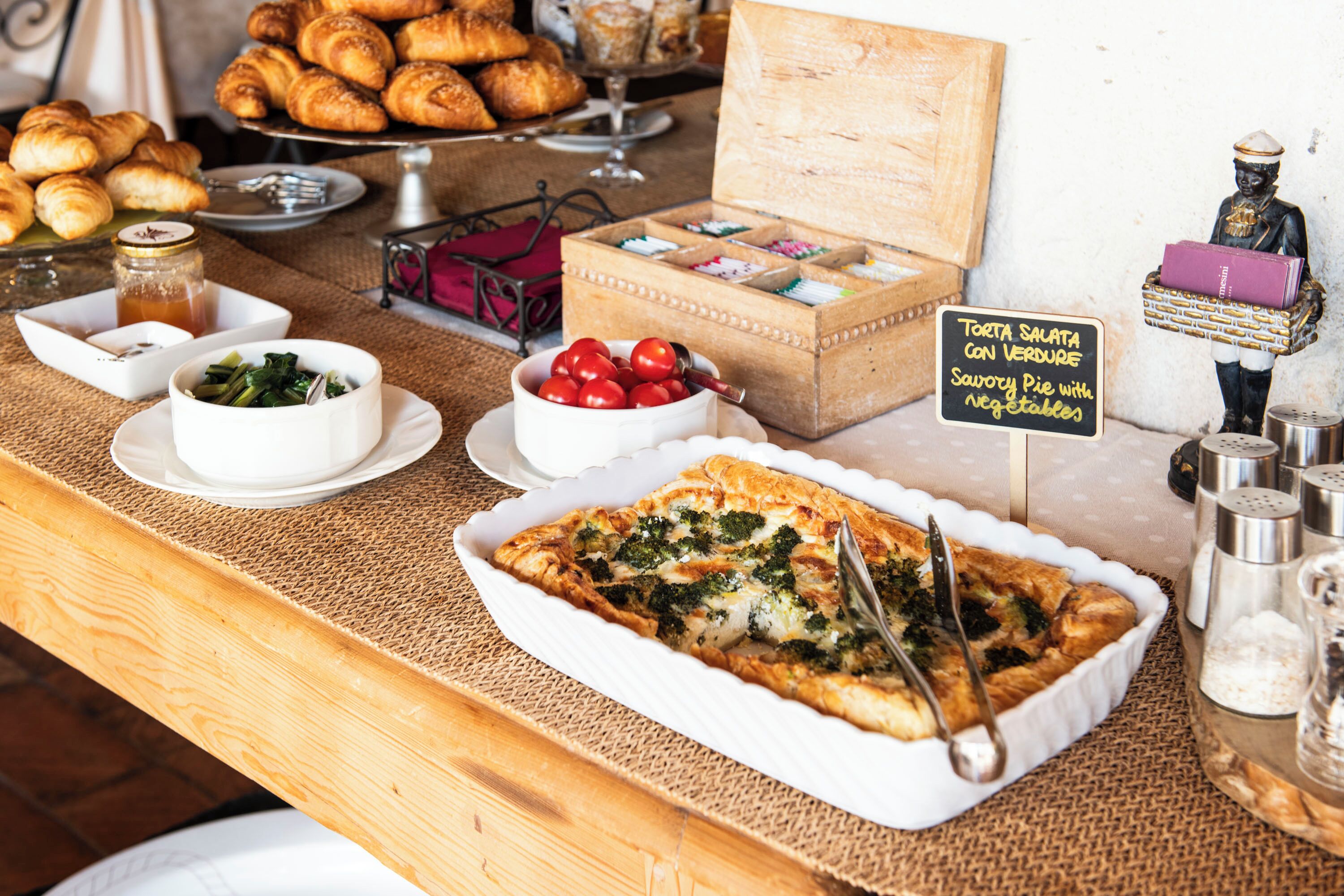 A buffet with various dishes including a large pie, vegetables, and pastries.