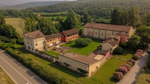 An aerial view of a historic building complex with multiple structures, a central courtyard, and surrounding greenery.