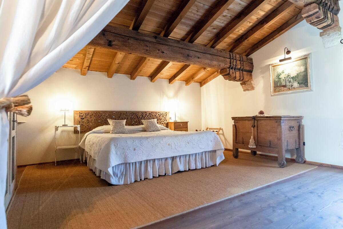 Ein Schlafzimmer mit Holzboden, einem Bett mit weißer Bettdecke, einem Nachttisch, einer Kommode und einem Bild an der Wand.