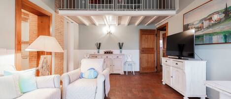 A spacious living area with a high ceiling, a balcony, a television, and a fireplace.