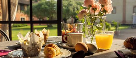Une table de petit-déjeuner avec des croissants, un verre de jus d’orange et un vase rempli de fleurs.