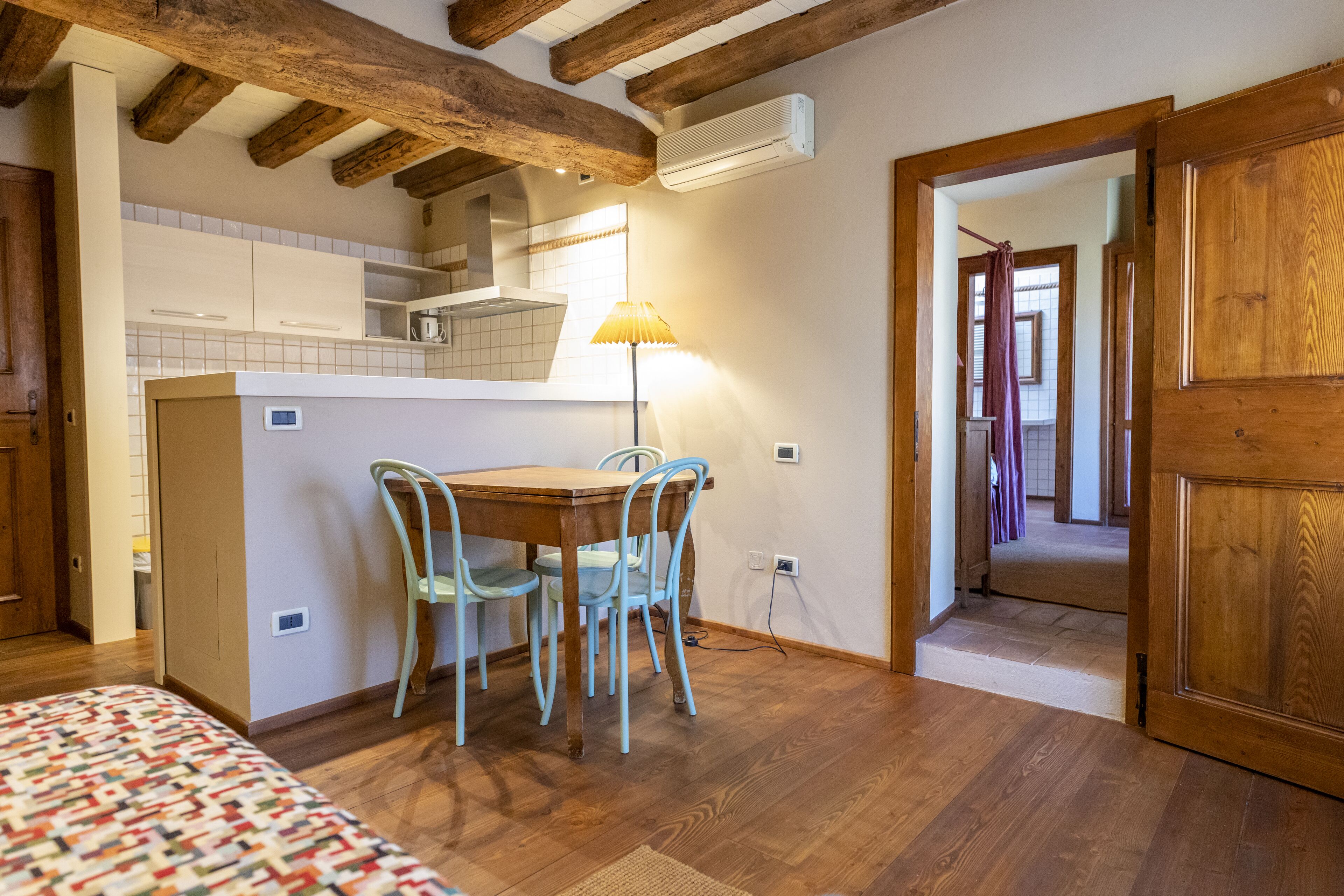 A cozy room with a wooden dining table, four chairs, a patterned bed, and exposed wooden beams on the ceiling.