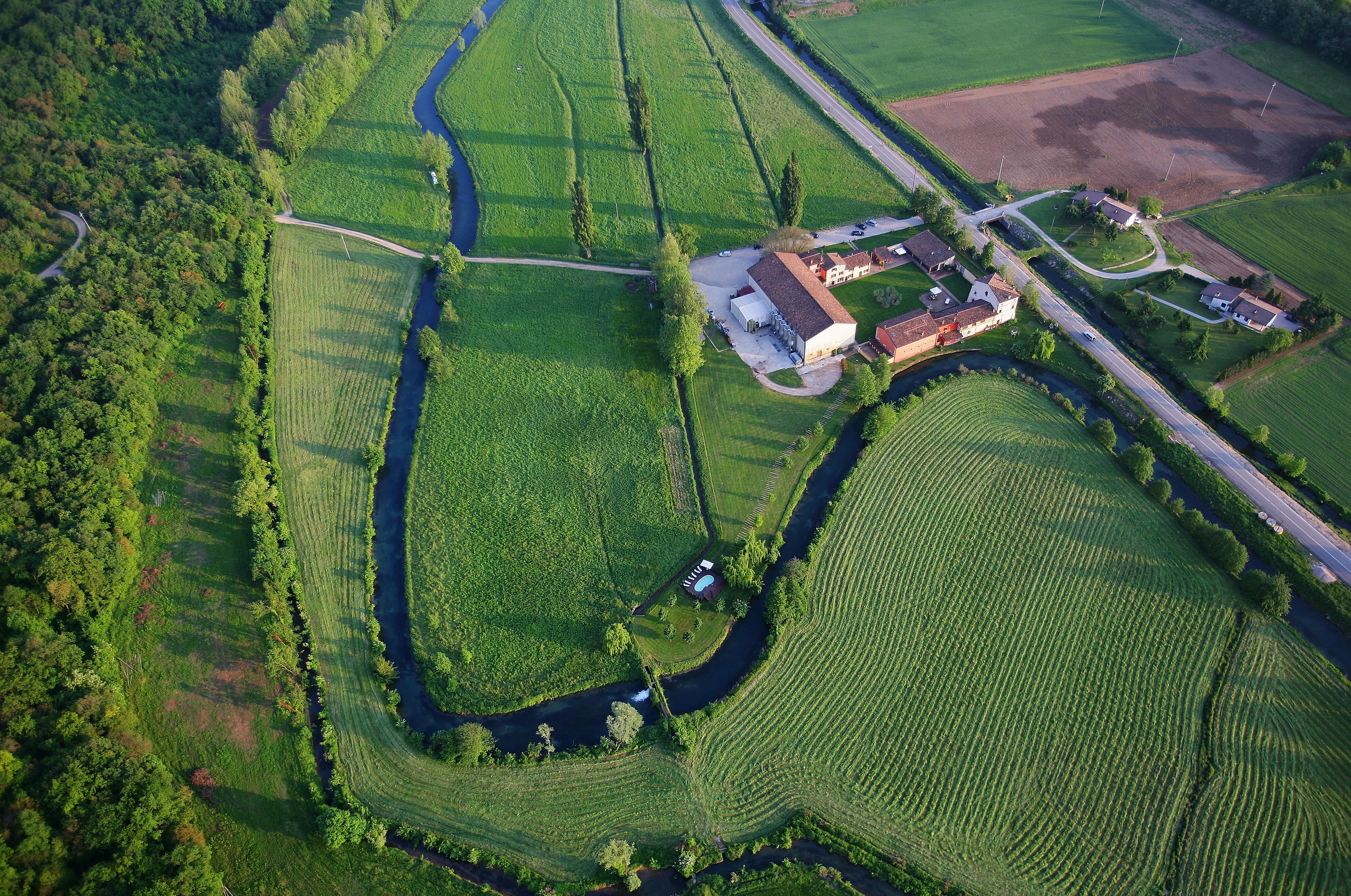 Vogelperspectief van een landelijk gebied met velden, een rivier en enkele gebouwen.