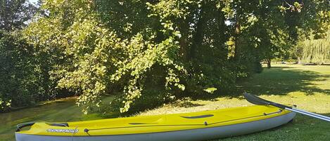 Una canoa amarilla con un remo en un área cubierta de césped, cerca de un cuerpo de agua rodeado de árboles.