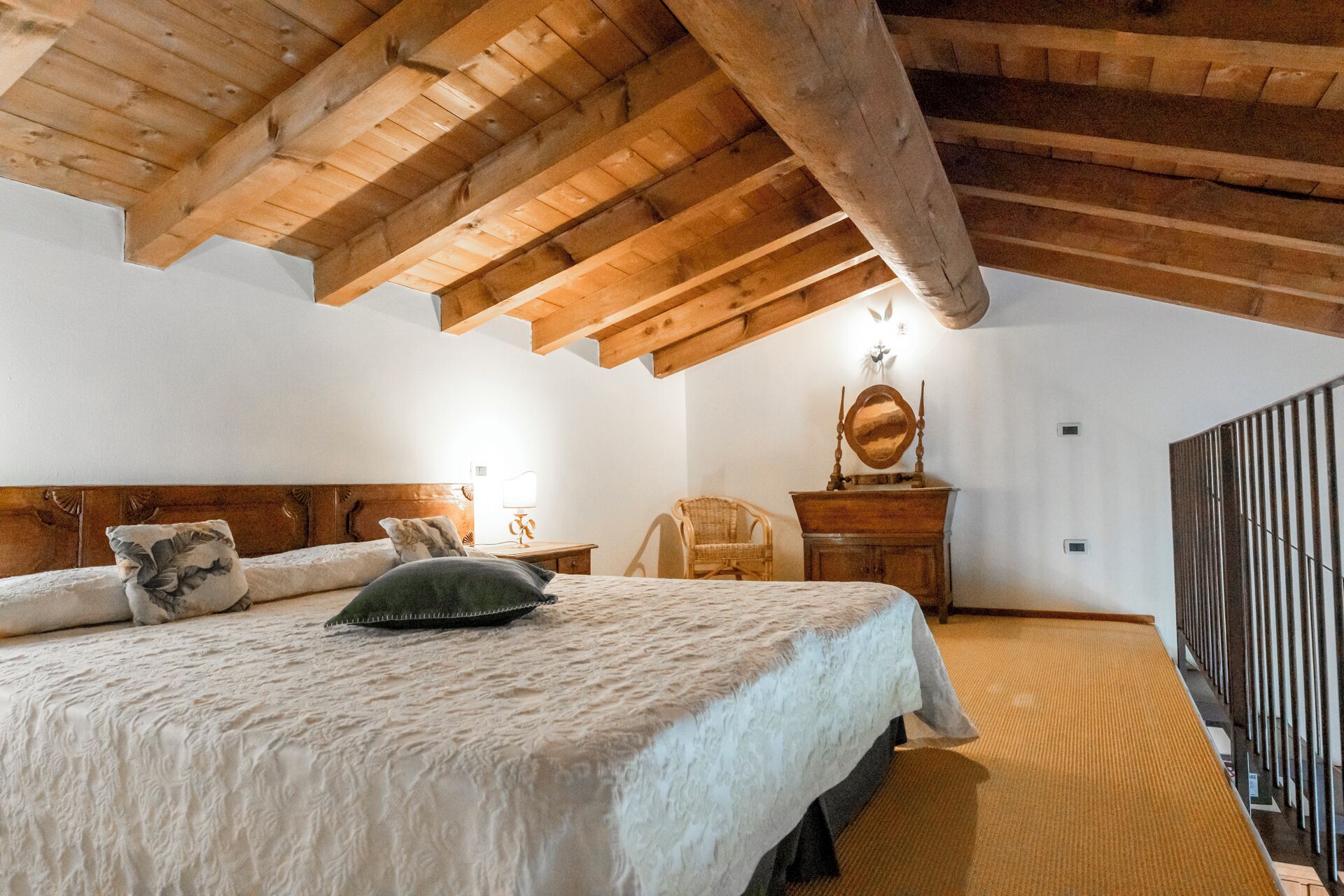 Un dormitorio con techo de madera, una cama con colcha blanca, una silla, un aparador y un espejo.