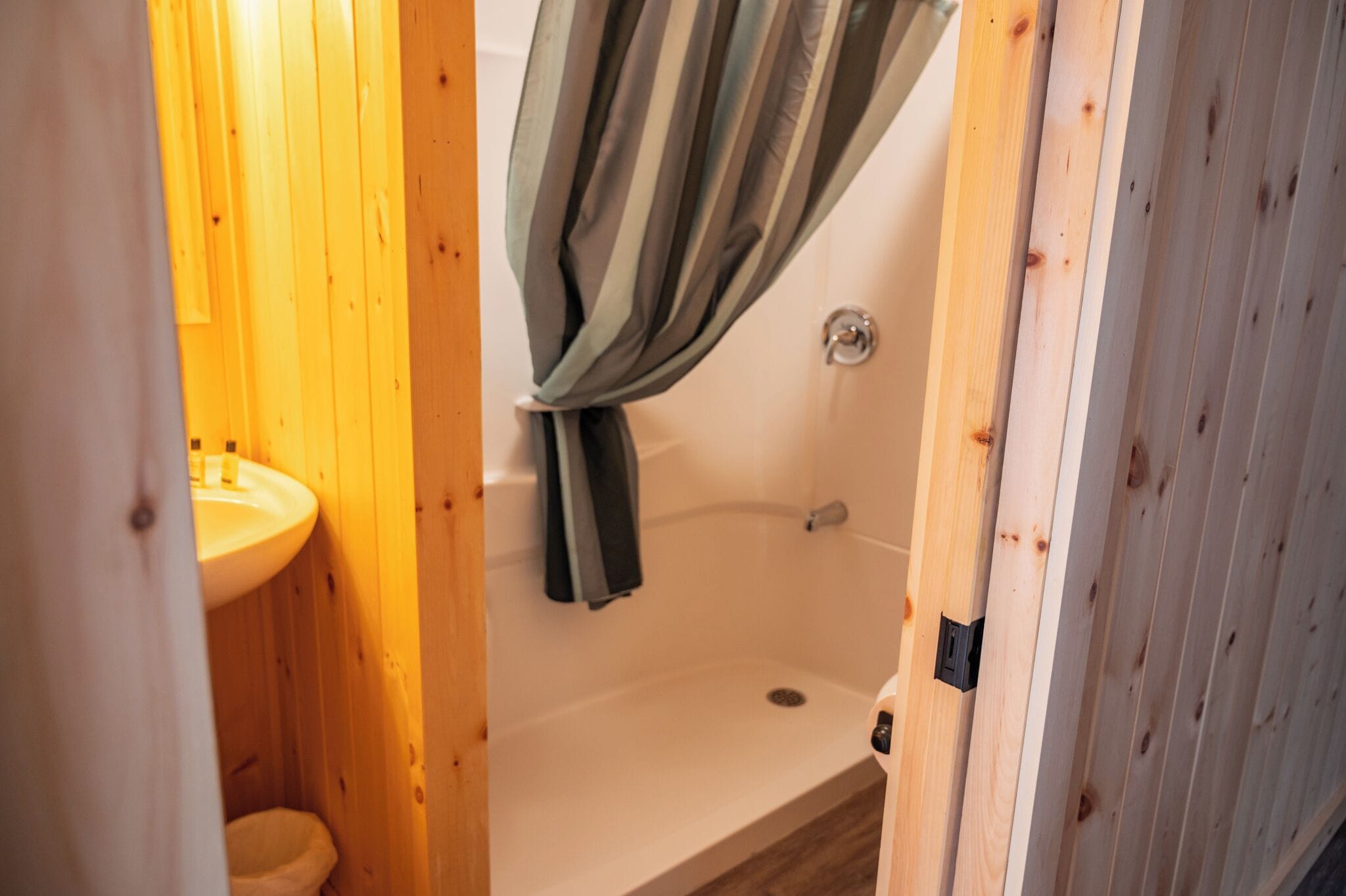 A wooden bathroom with a white sink, a shower, and a curtain.