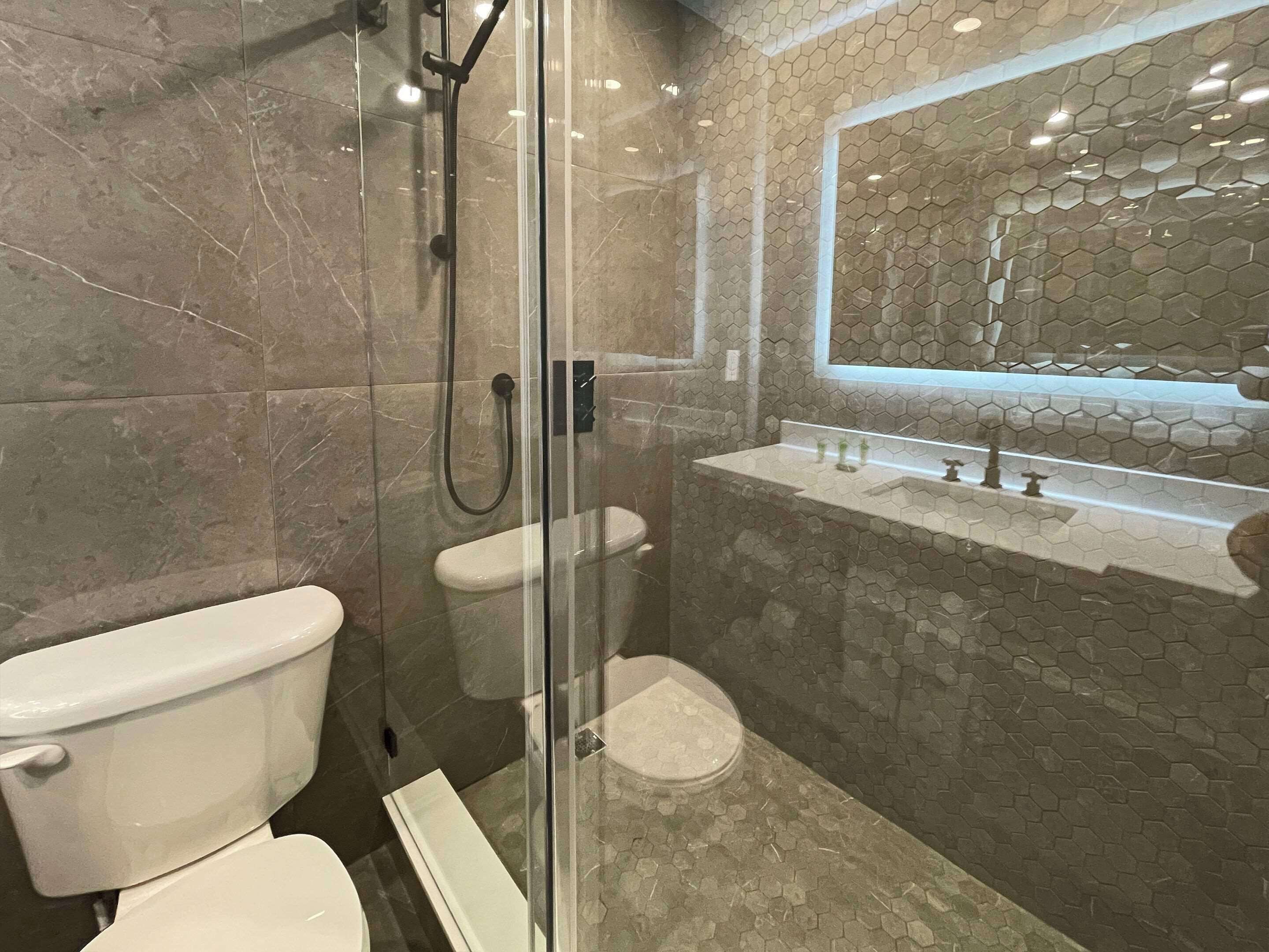 Un baño moderno con cabina de ducha de vidrio, inodoro y lavamanos con salpicadero de azulejos hexagonales.