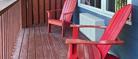 Una terraza de madera con dos sillas Adirondack rojas y una unidad de aire acondicionado blanca.