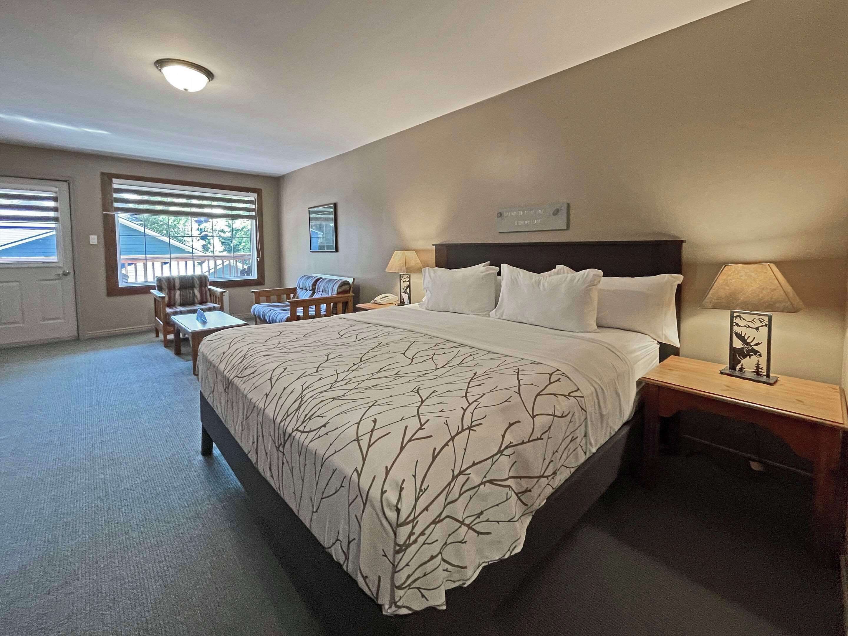 Una habitación de hotel con una cama grande, dos mesitas de noche con lámparas, una silla, un escritorio y una ventana con persianas.