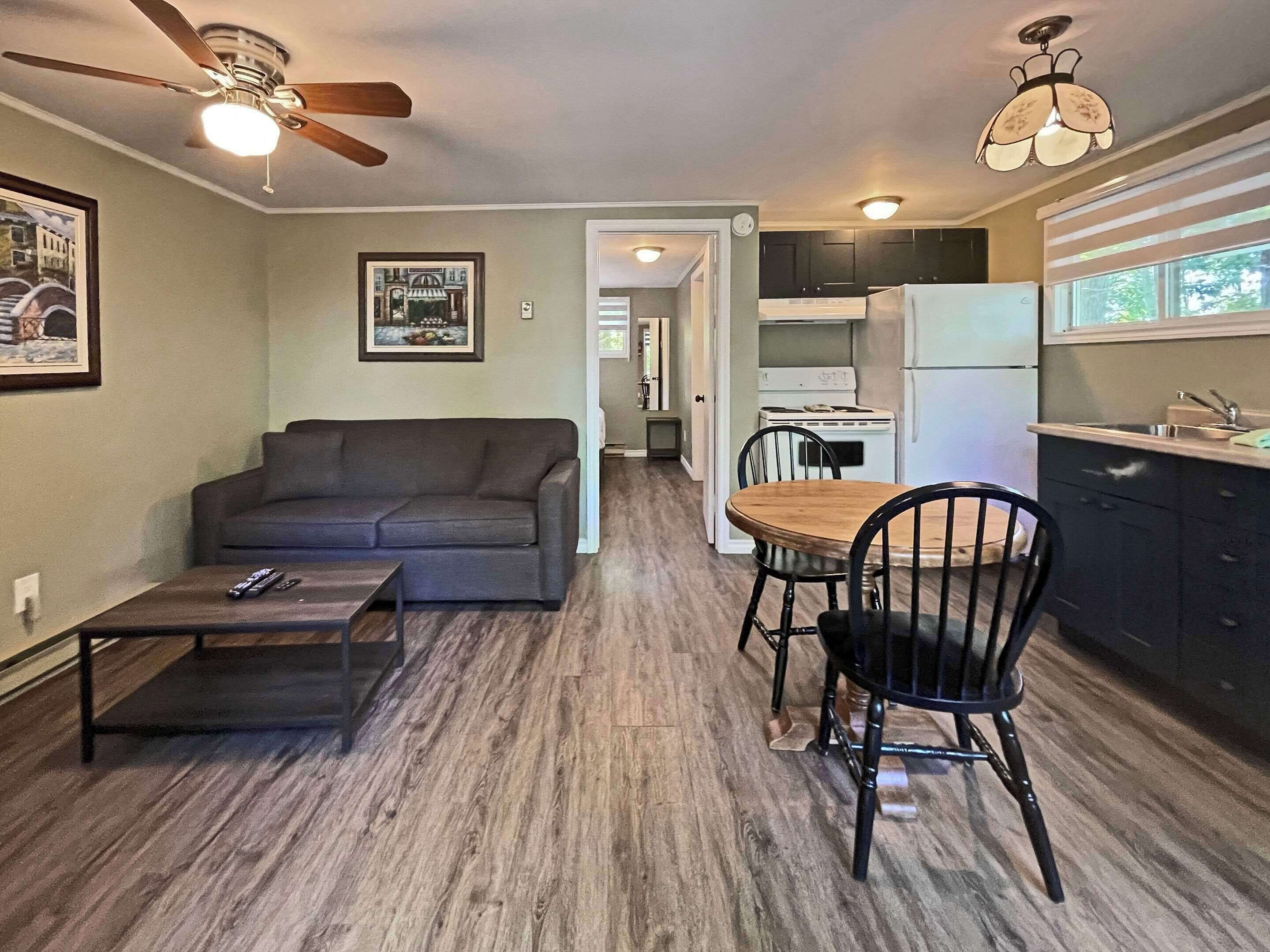 A compact living space with a sofa, dining table, chairs, a kitchen area with a refrigerator, and a ceiling fan.