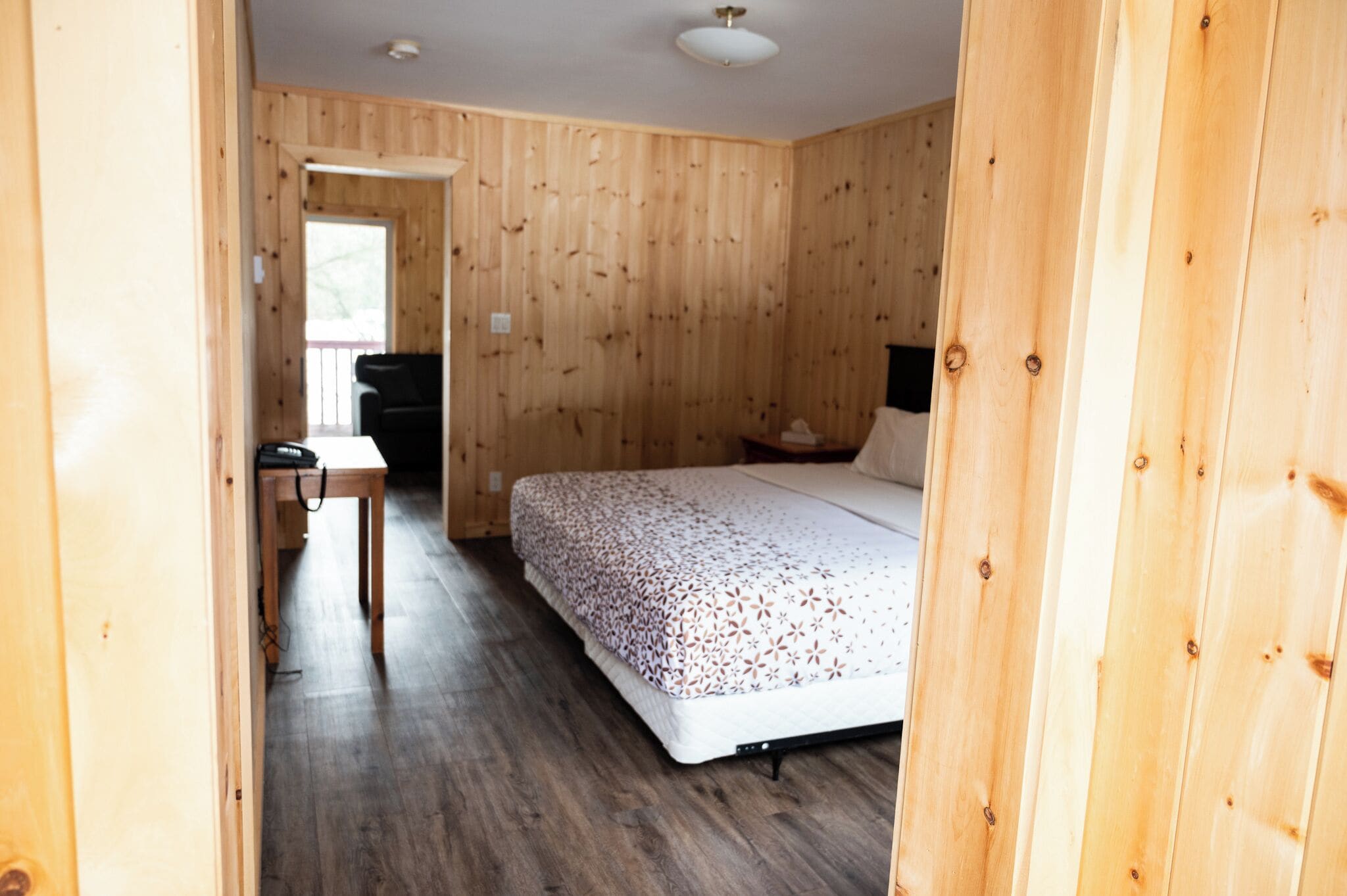 A wooden-paneled room with a bed, a desk, and a chair.