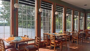 Un restaurante con grandes ventanales que ofrecen vistas a un lago, muebles de madera y suelo de baldosas.