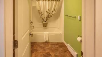 Un baño con bañera, cortina de ducha, toalla, soporte para papel higiénico y radiador.