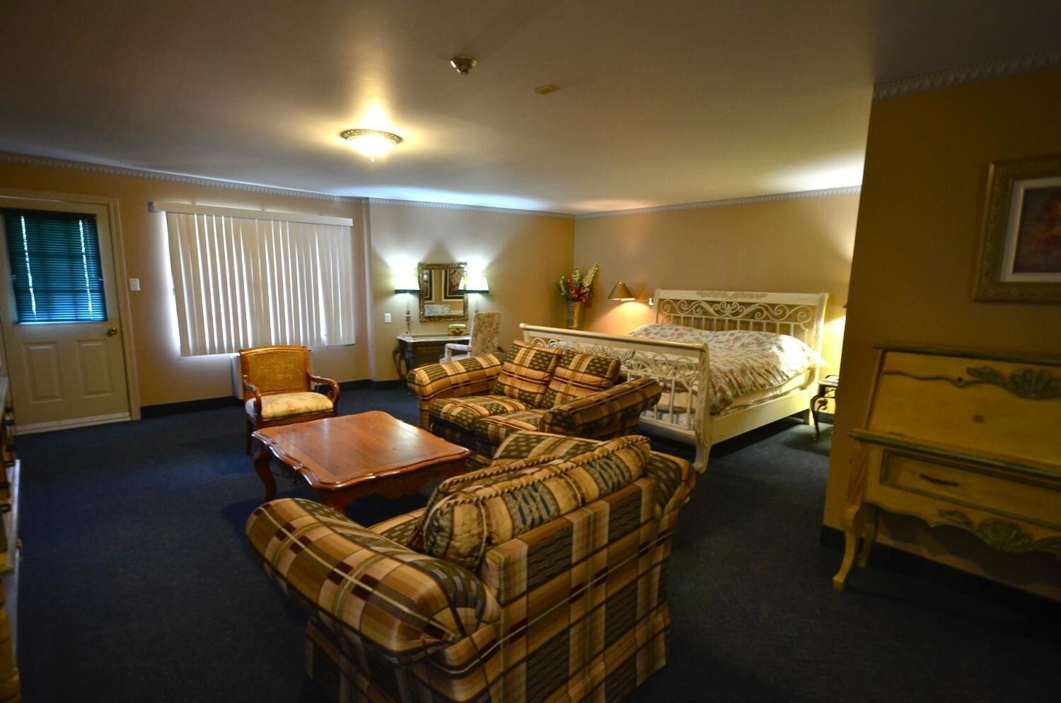 Ein Hotelzimmer mit einem Bett, zwei Sesseln, einem Sofa, einem Holztisch, einem Nachttisch und einer Lampe.