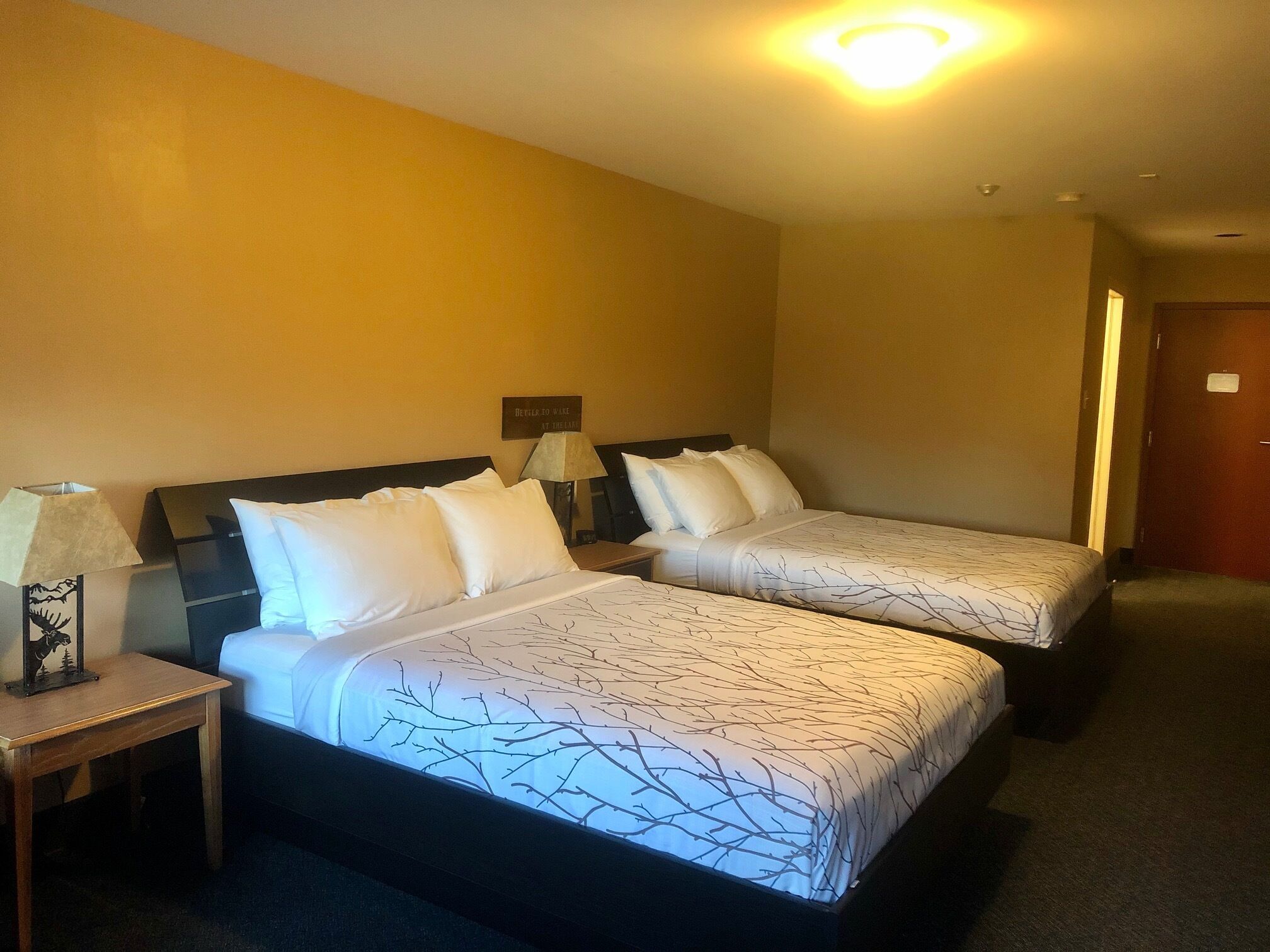 Una habitación de hotel con dos camas, cada una con una colcha estampada, una mesita de noche con lámpara y un cartel en la pared.