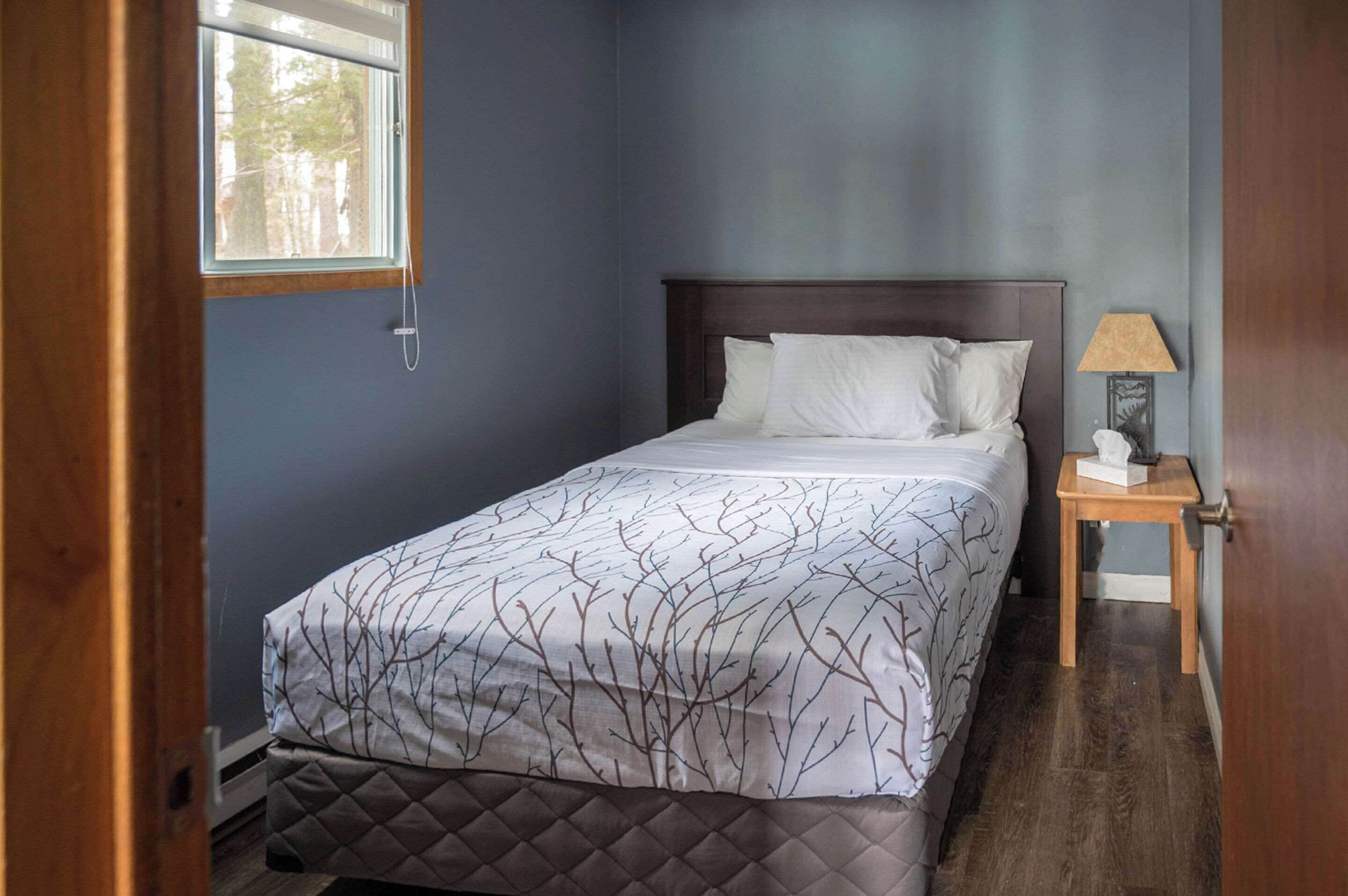 Une chambre à coucher avec un lit, une table de chevet, une lampe et une fenêtre.