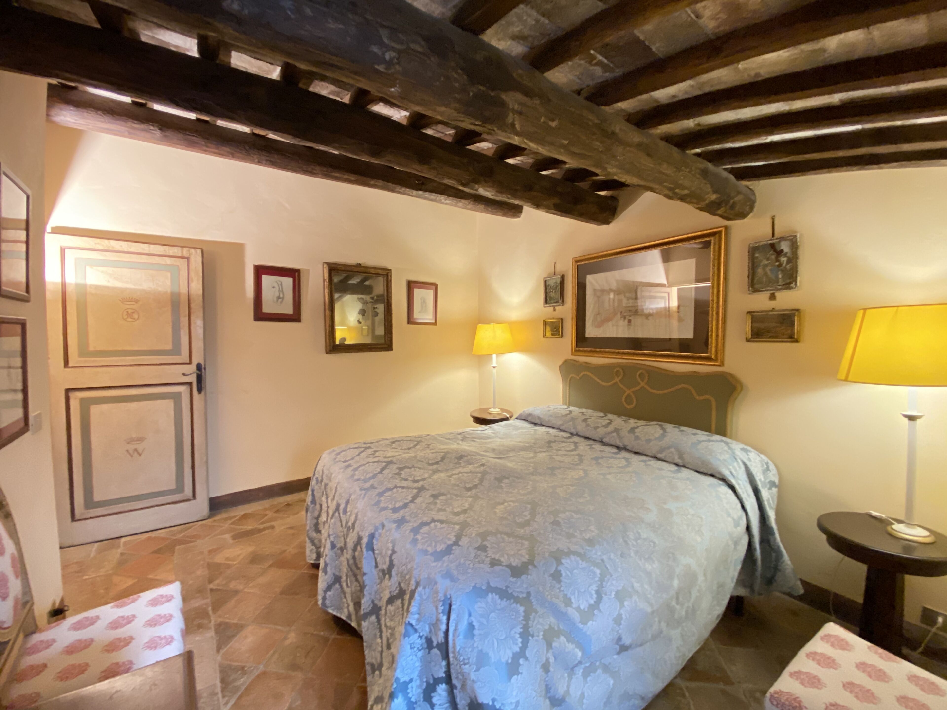 Un dormitorio con cama, mesita de noche, lámpara y puerta con escudo heráldico.