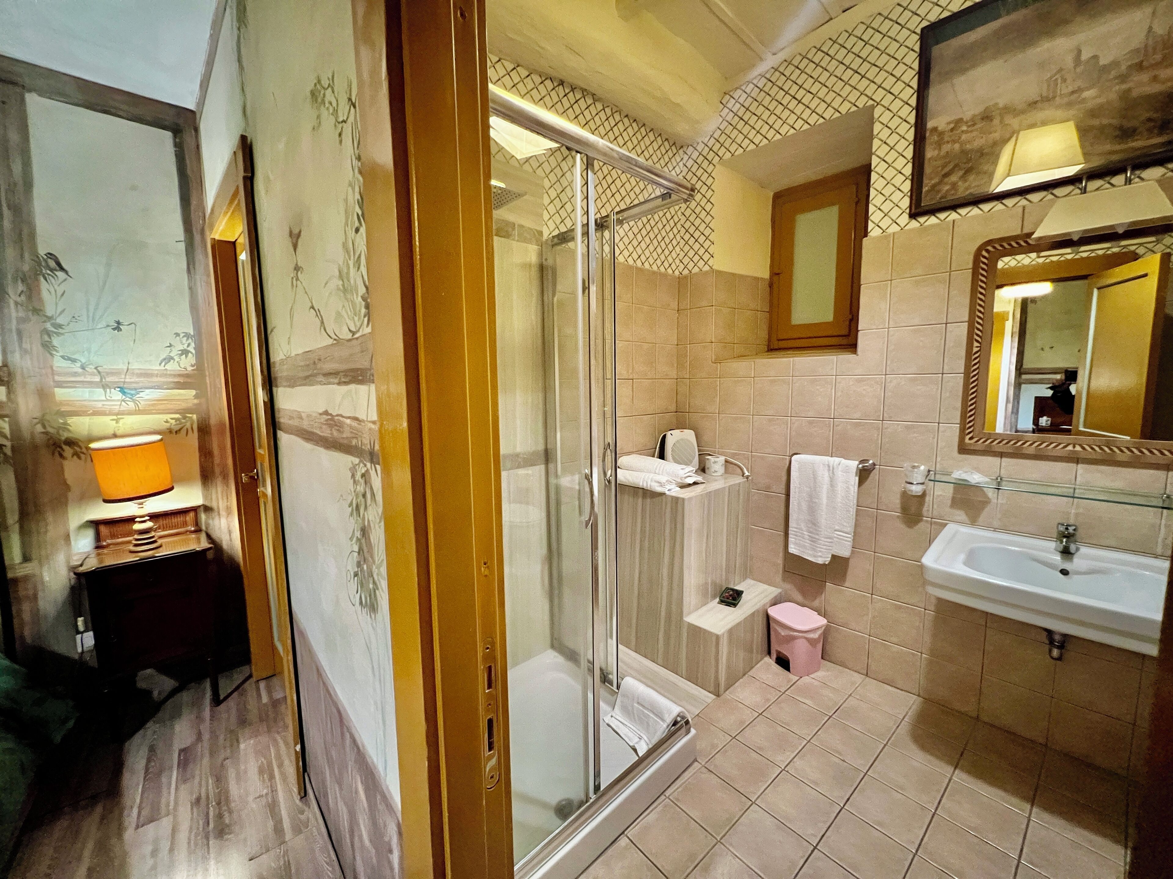 A bathroom with a glass shower enclosure, a sink, a mirror, and a towel rack.