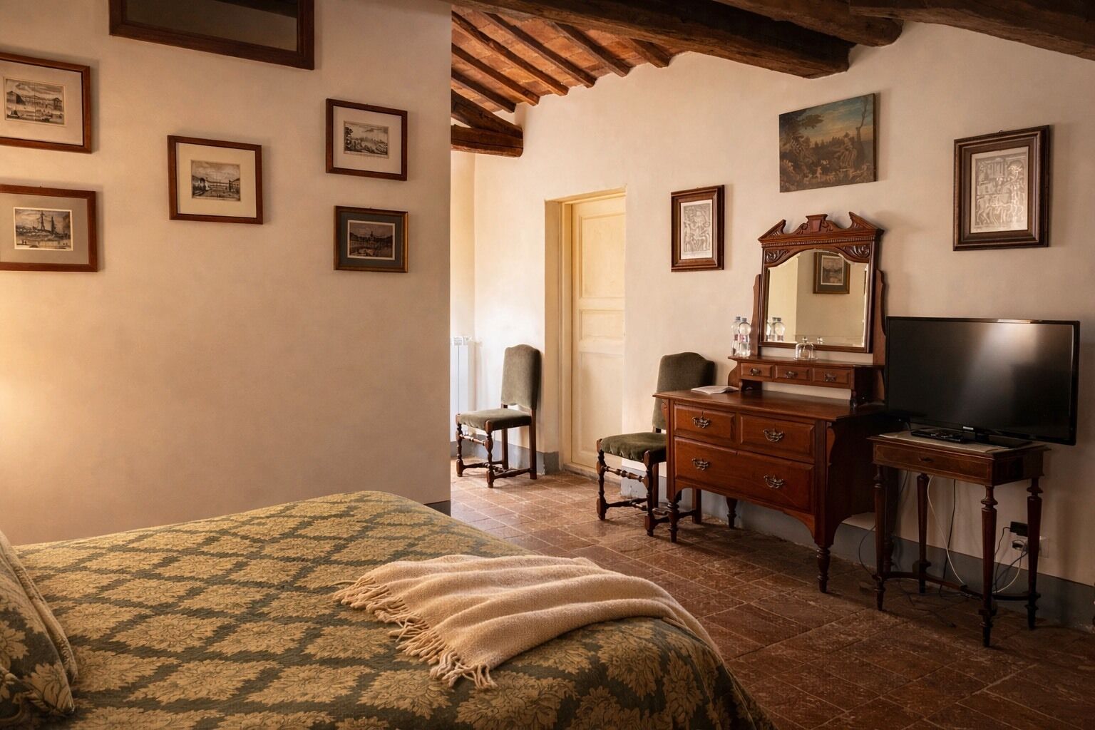 A room with a bed, a wooden dresser, a chair, a television, and several framed pictures on the wall.