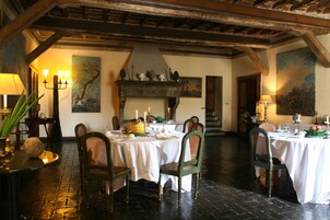 A dining area with two tables set for a meal, wooden chairs, a chandelier, and a fireplace.