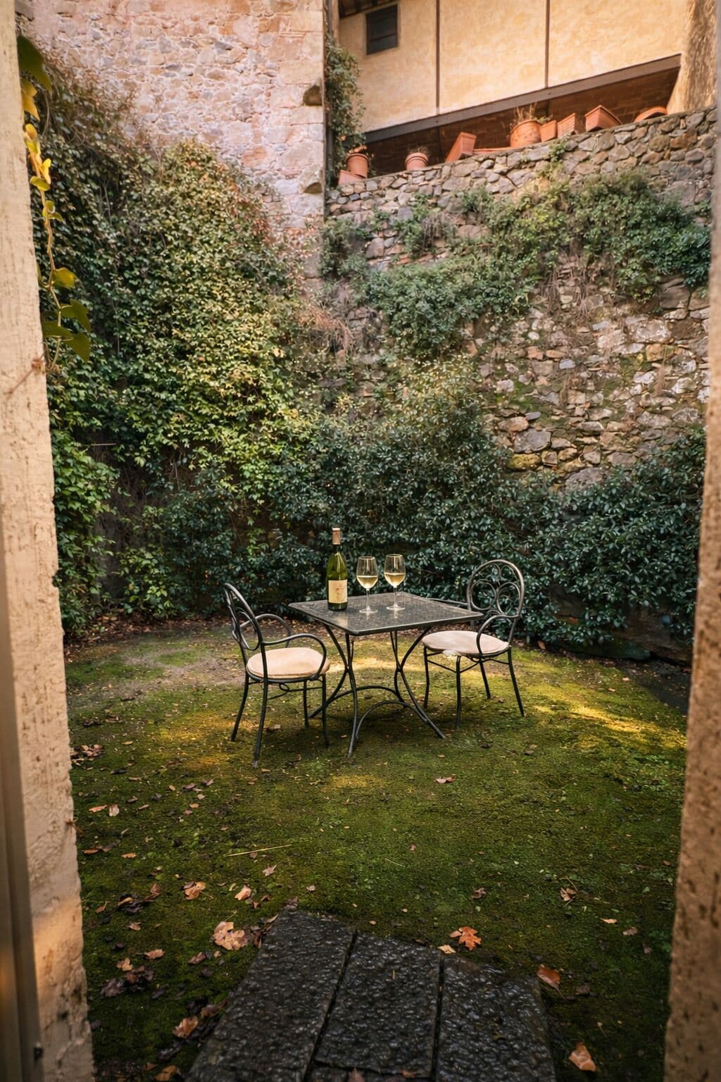 A stone wall with a small table and chairs in a garden area.