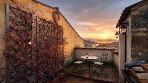 Un patio exterior acogedor con una mesa y sillas, rodeado por un muro cubierto de plantas trepadoras, con vistas a un paisaje pintoresco.