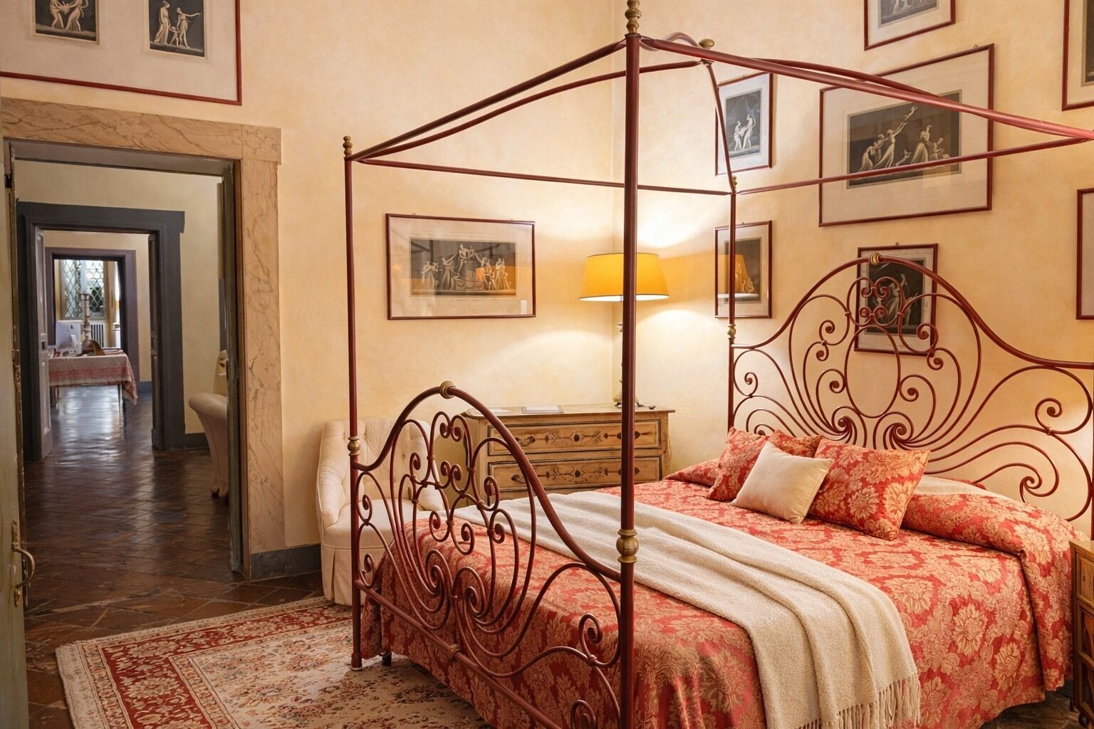 Un lit à baldaquin avec une couvre-lit à motifs rouges et blancs, une table de chevet en bois avec une lampe et un sol en marbre.