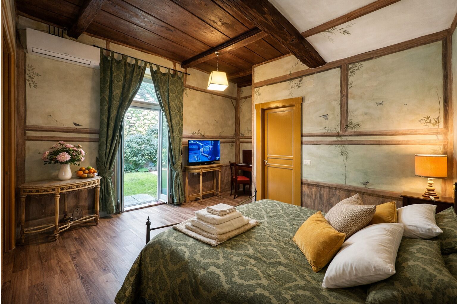 A room with a bed, a television, a table with flowers, and a door.