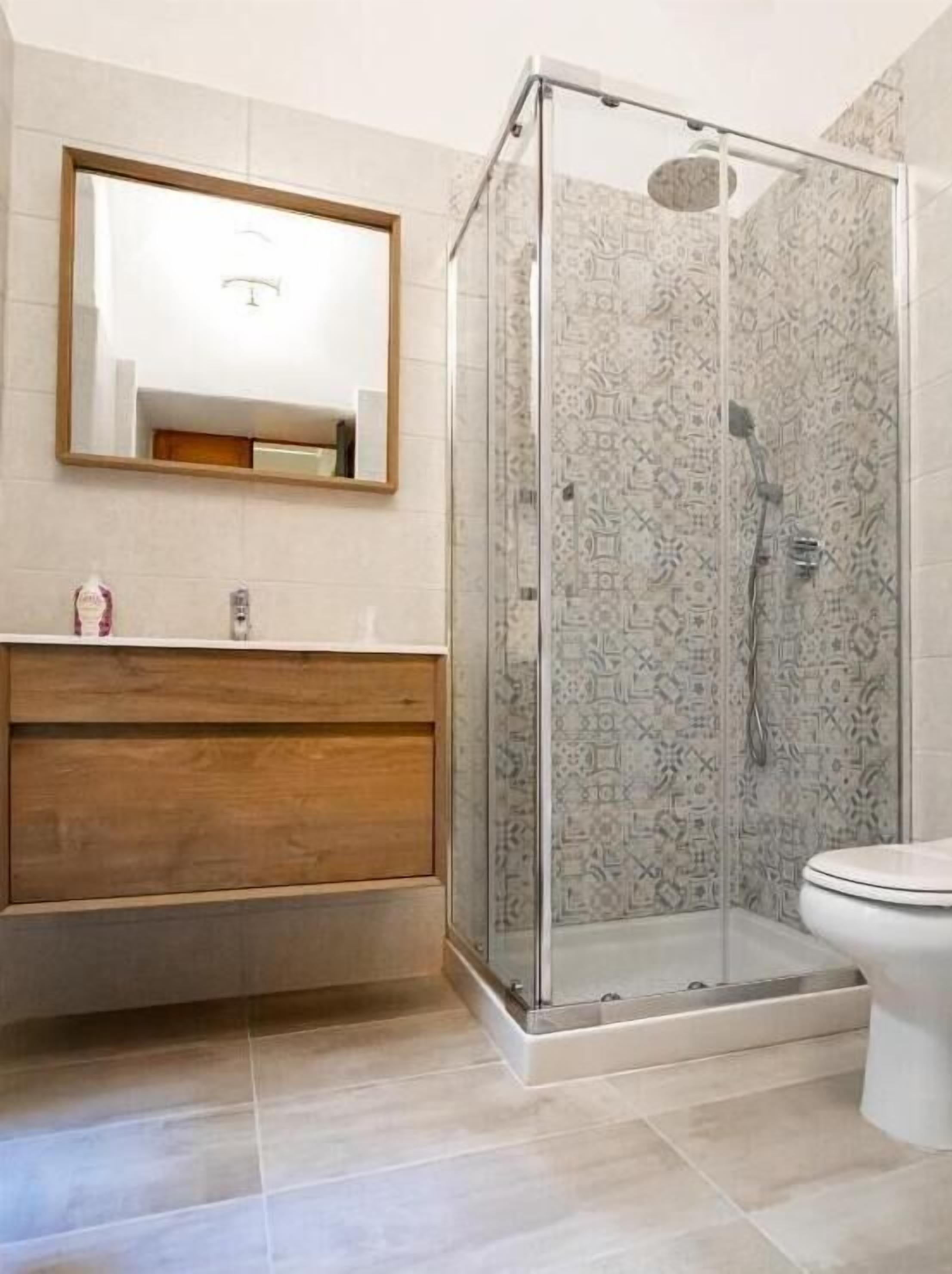Un baño con cabina de ducha de vidrio, tocador de madera, inodoro y espejo.
