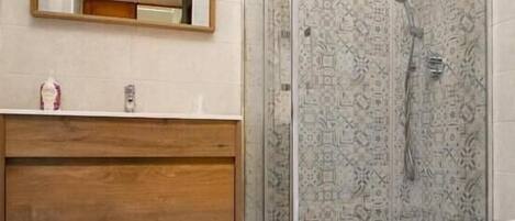 Un baño con cabina de ducha de vidrio, tocador de madera, inodoro y espejo.