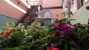 A narrow alleyway with a staircase leading to a building, a water fountain, and flowering plants.