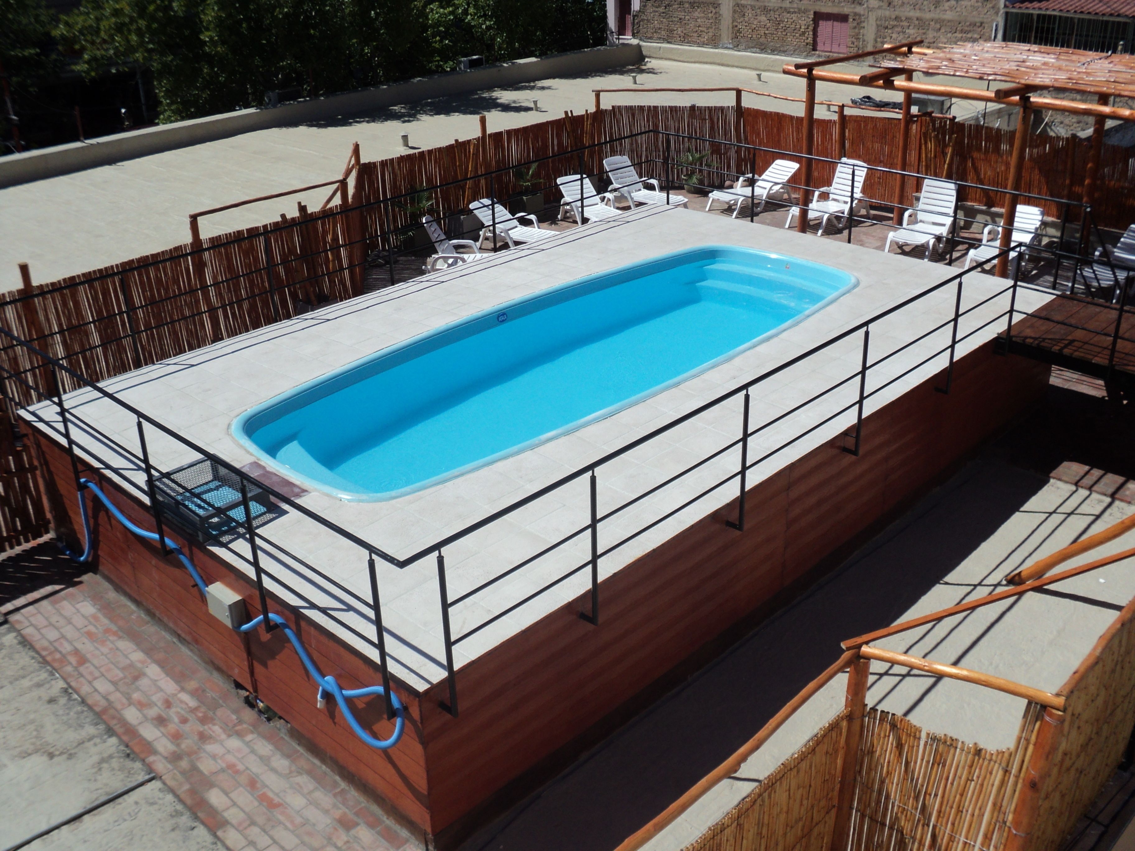 Piscina rectangular con un borde de baldosas, rodeada por una valla de madera y sillas reclinables blancas.