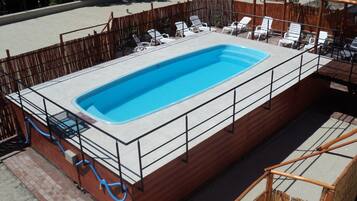 Piscina rectangular con un borde de baldosas, rodeada por una valla de madera y sillas reclinables blancas.