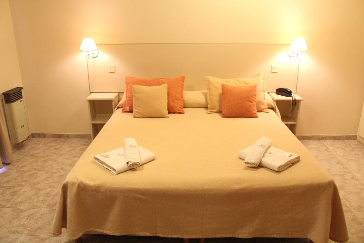 Une chambre d’hôtel comprenant un lit, deux tables de chevet et deux lampes fixées au mur.
