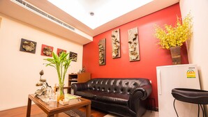 A living room with a black leather sofa, a wooden coffee table, and a red accent wall with decorative art. - Triple 8 Inn Bangkok (Bangkok)
