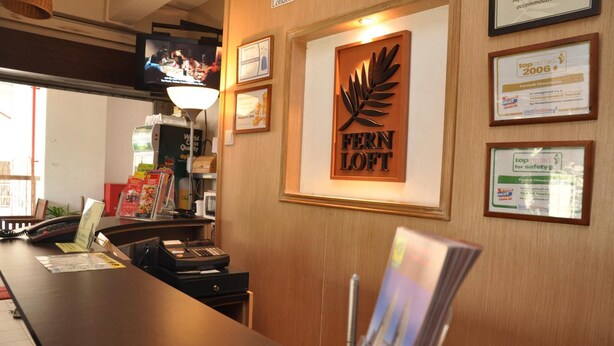 A reception desk with a Fern Loft sign, framed awards, and a television screen. - Fernloft Chinatown - Hostel (Singapore)