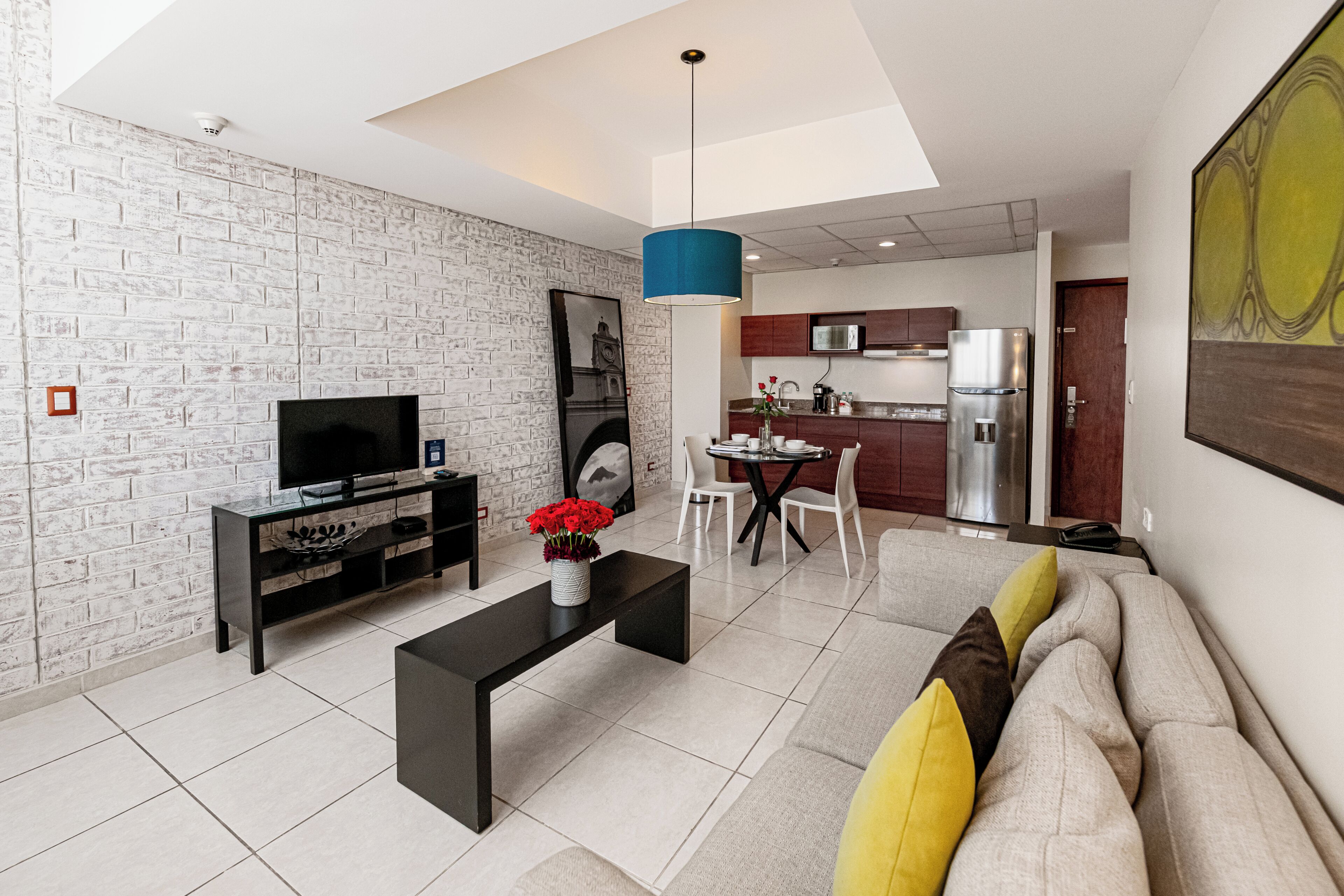 Una sala de estar moderna con televisor, mesa de centro negra y un sofá con cojines.