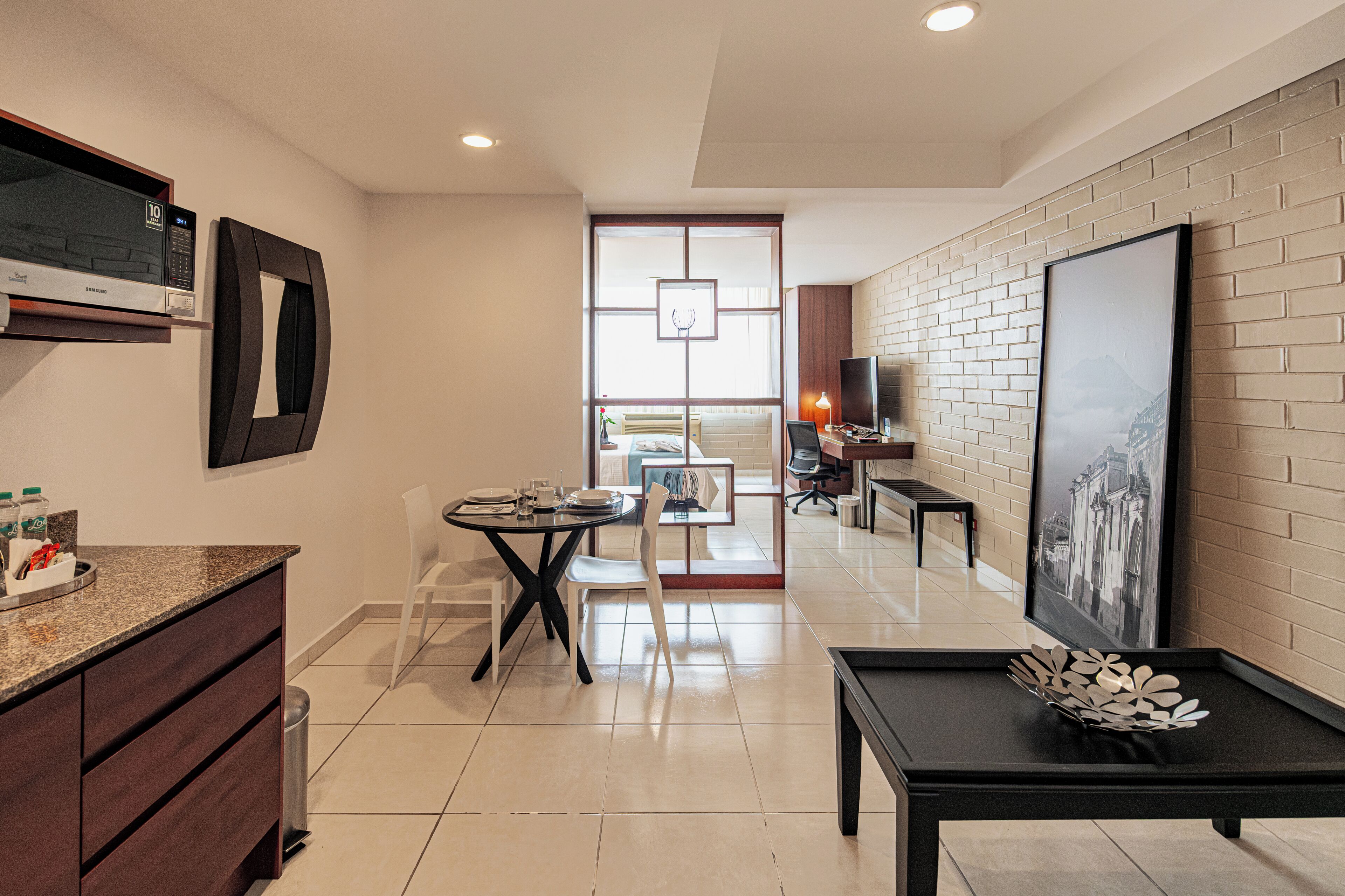 Una cocina moderna con microondas, un comedor con mesa y sillas, una mesa de centro negra y un cuadro grande en la pared.