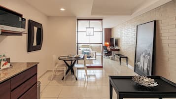 A modern kitchen with a microwave, a dining area with a table and chairs, a black coffee table, and a large framed picture on the wall.
