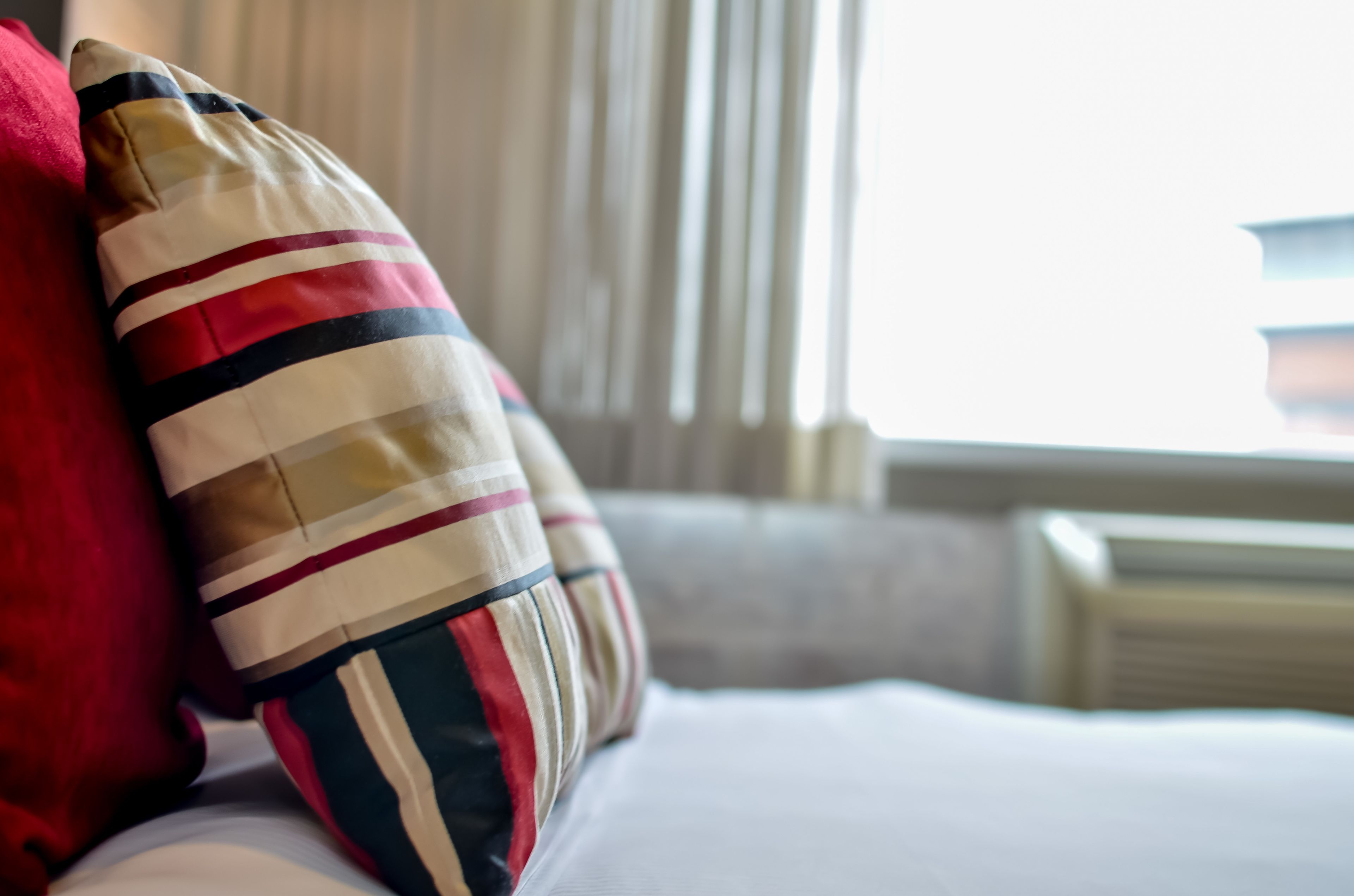 A bed with striped pillows and a red pillow.