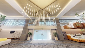 A modern hotel lobby with a central reception desk, a large chandelier, and potted plants.