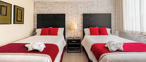 A hotel room with two beds, a brick wall, a nightstand with a lamp, and a window with curtains.