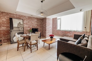 A living room with a brick wall, a dining area with a table and chairs, a sofa, and a television. - Adriatika Hotel & Residence (Guatemala City)