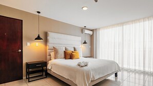 A modern hotel room with a large bed, bedside tables, a wardrobe, and a window with curtains.