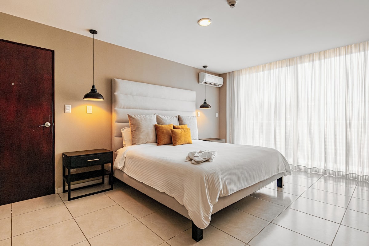A modern hotel room with a large bed, bedside tables, a wardrobe, and a window with curtains.