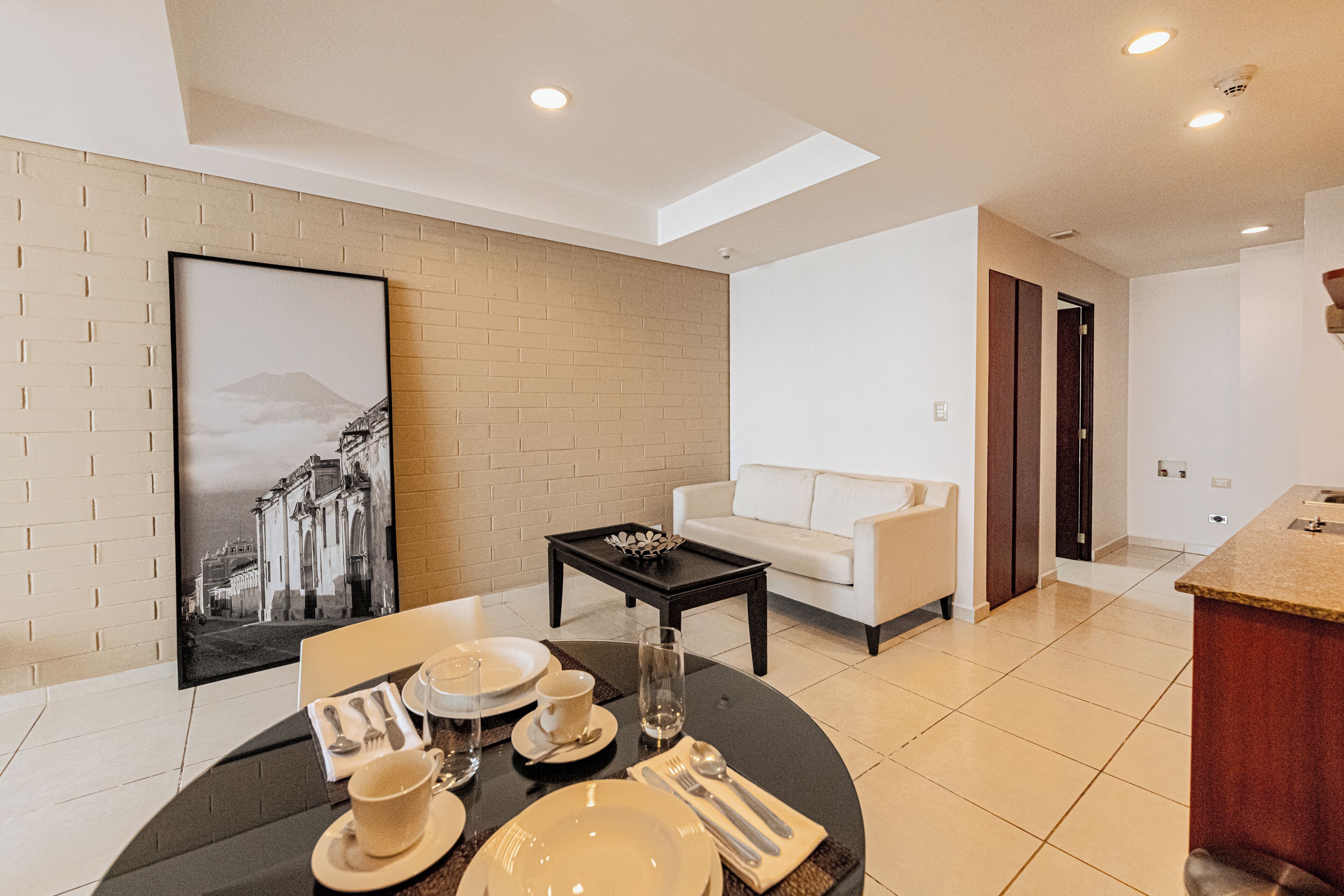 A modern living room with a dining area, a white sofa, a black coffee table, and a large framed picture on the wall.