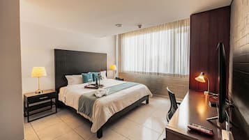 A hotel room with a bed, bedside tables, a desk with a lamp, a TV, and a window with curtains.