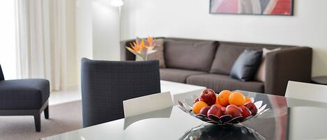 Una sala de estar moderna con una mesa de comedor de cristal, un frutero y un sofá marrón.